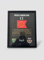 Framed plaque with 'Proud Americans' text and various insignias held by a person.